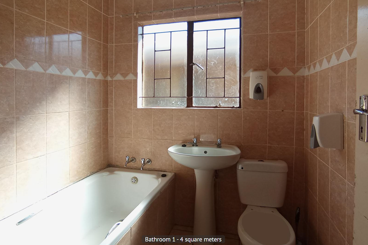 A functional bathroom featuring a bathtub, pedestal basin, and toilet with full-height wall tiling and a window for natural light.