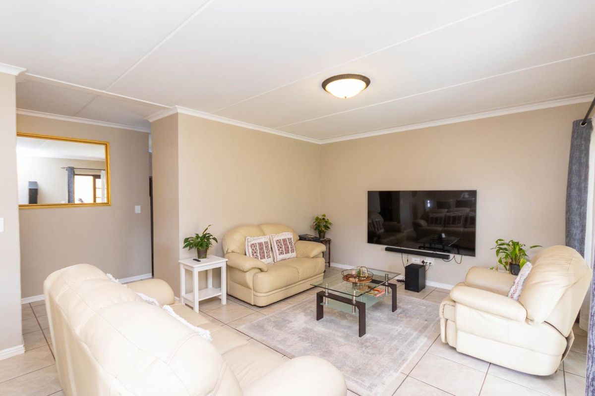A comfortable living room featuring neutral wall tones, tiled flooring, and a coved ceiling, providing a functional and well-lit space for relaxation.