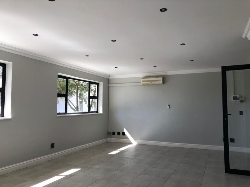 A bright, empty office space featuring neutral grey walls, tiled flooring, recessed lighting, and a wall-mounted air conditioning unit.