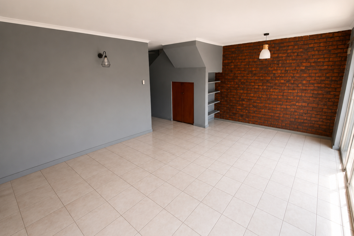 Spacious living area featuring a striking exposed brick wall, neutral tiled flooring, and convenient built-in under-stair storage with integrated shelving.