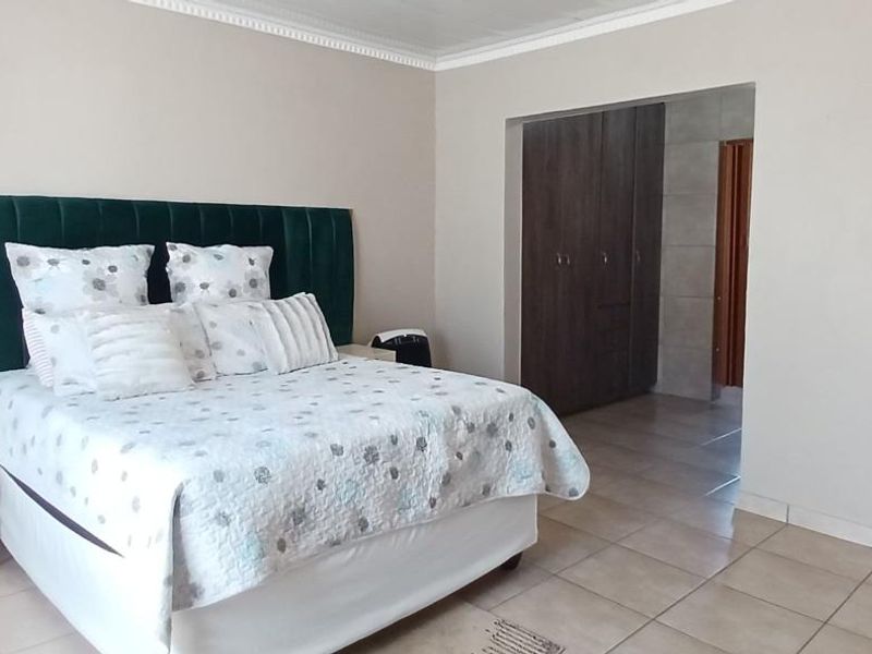 Spacious bedroom featuring neutral wall tones, tiled flooring, decorative cornice, and integrated built-in cupboards for storage.