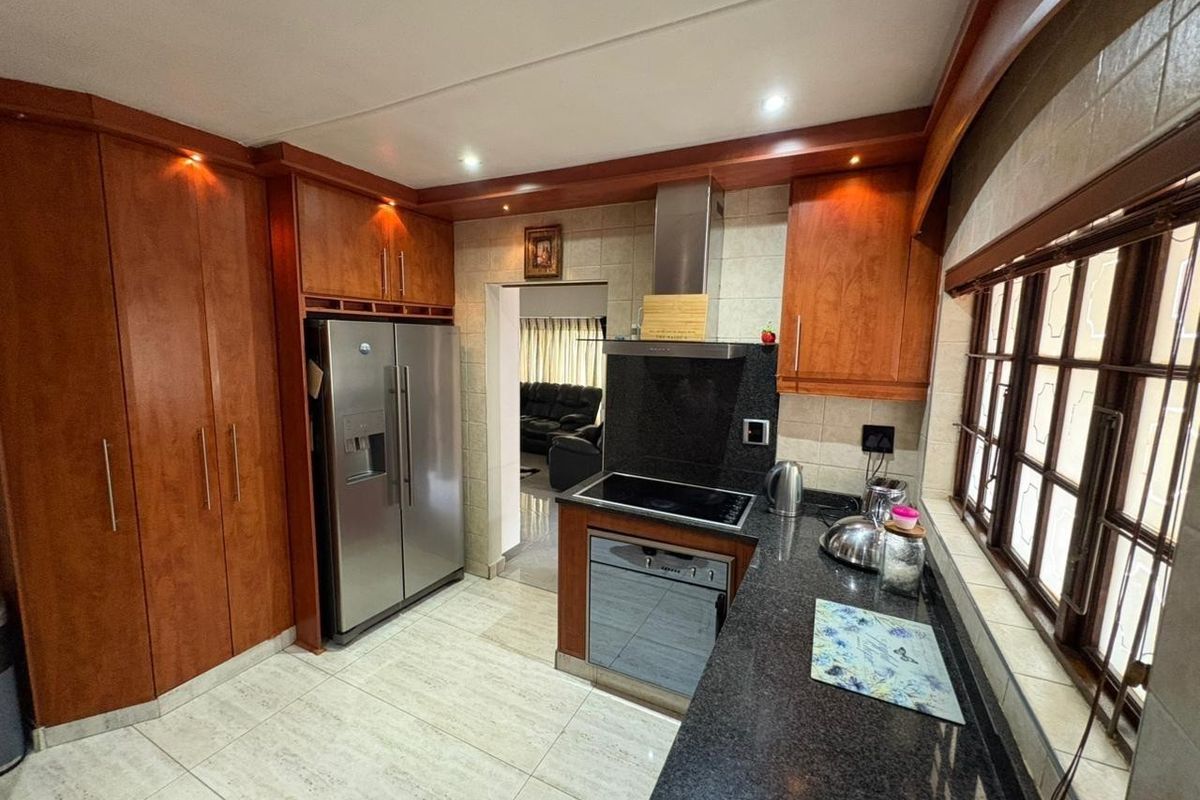 A functional kitchen featuring warm-toned wooden cabinetry, dark granite countertops, integrated appliances, and tiled flooring with recessed lighting.