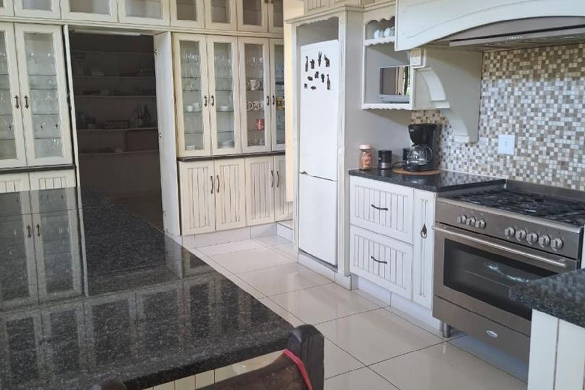 Spacious kitchen featuring cream-toned cabinetry, granite countertops, a large central island, and a dedicated walk-in pantry area with extensive shelving.