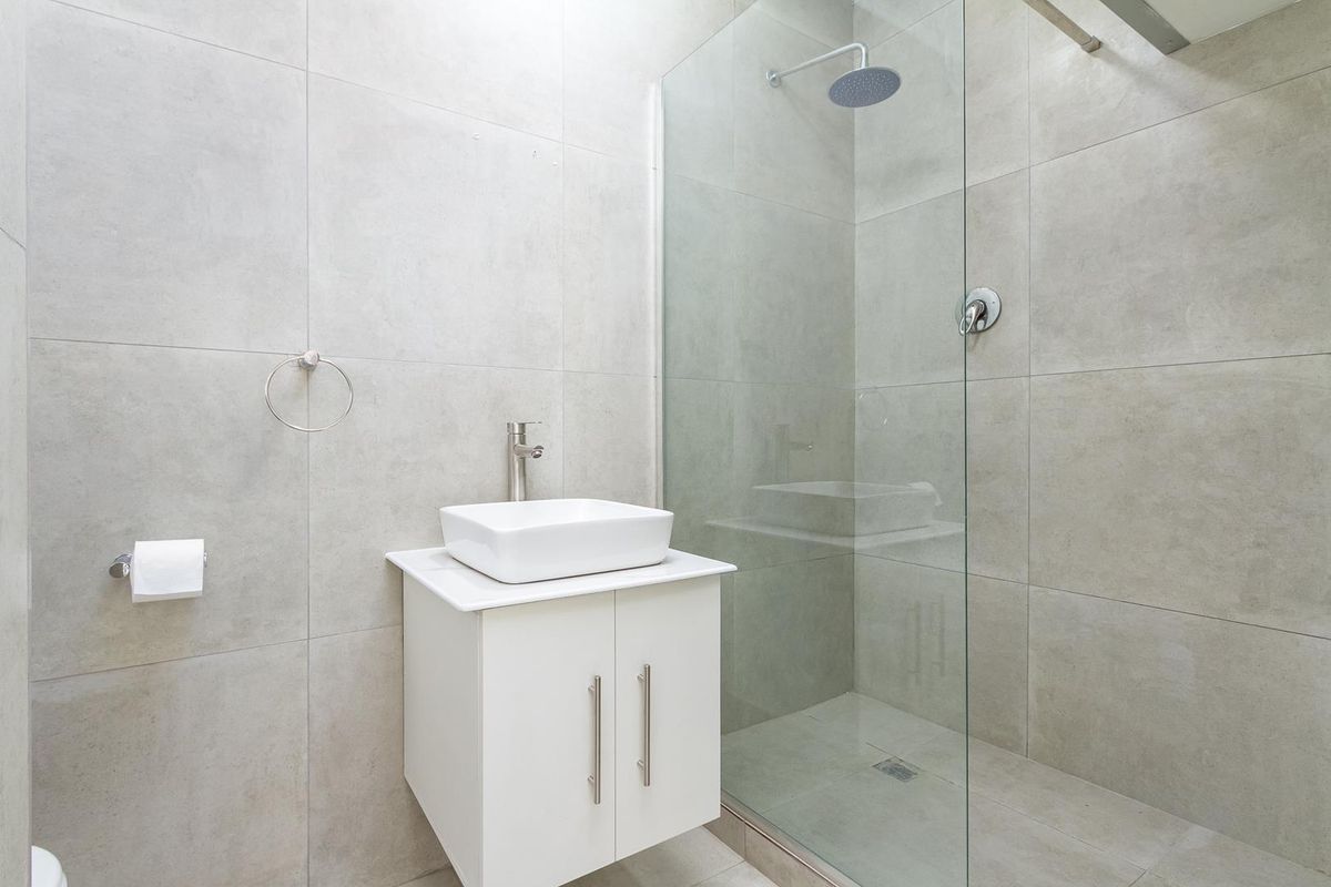 Modern bathroom featuring large format grey tiling, a wall-mounted vanity with a vessel sink, and a spacious walk-in shower with a rainfall shower head.