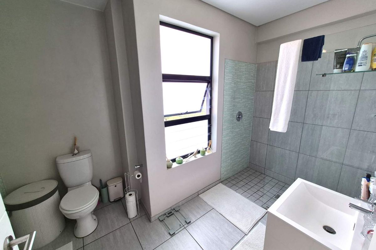 A modern bathroom featuring a walk-in shower with tiled walls, a wall-mounted basin, and a toilet, finished with neutral floor tiles.