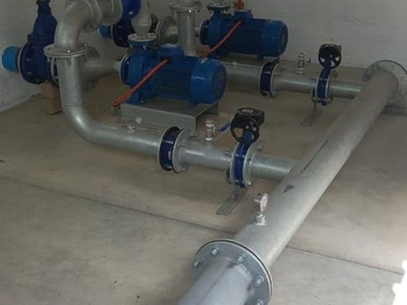 A functional utility space housing a well-maintained industrial water pump system with exposed piping and valves.