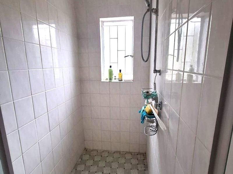 A functional shower enclosure featuring tiled walls and flooring, equipped with a standard shower mixer and a window with security bars.