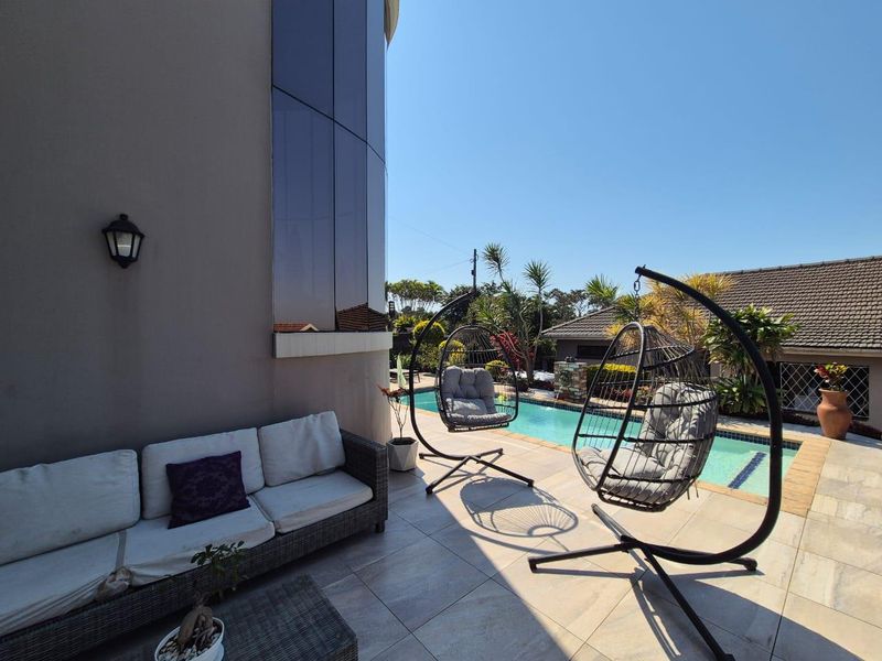 A well-maintained outdoor patio area featuring tiled flooring, a swimming pool, and a modern curved glass exterior wall.