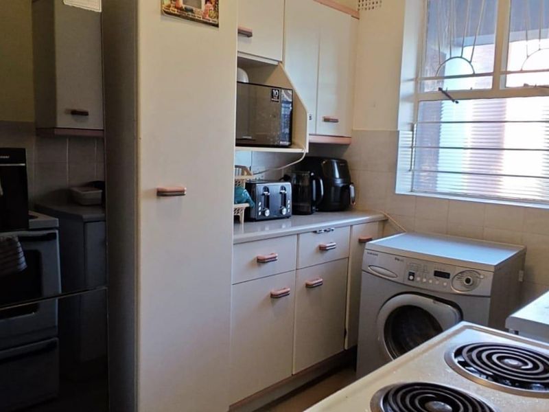 Functional kitchen featuring built-in cabinetry, laminate countertops, electric stove, and dedicated space for a washing machine with tiled splashback.