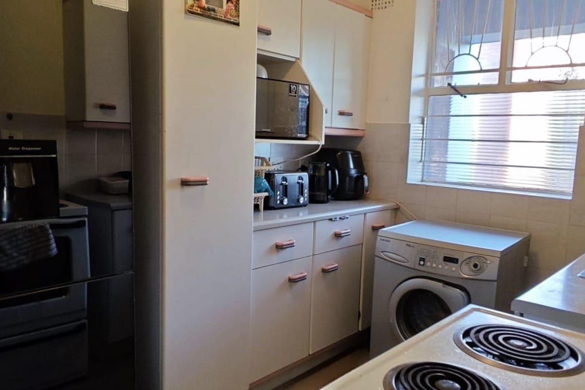 Functional kitchen featuring built-in cabinetry, laminate countertops, electric stove, and dedicated space for a washing machine with tiled splashback.