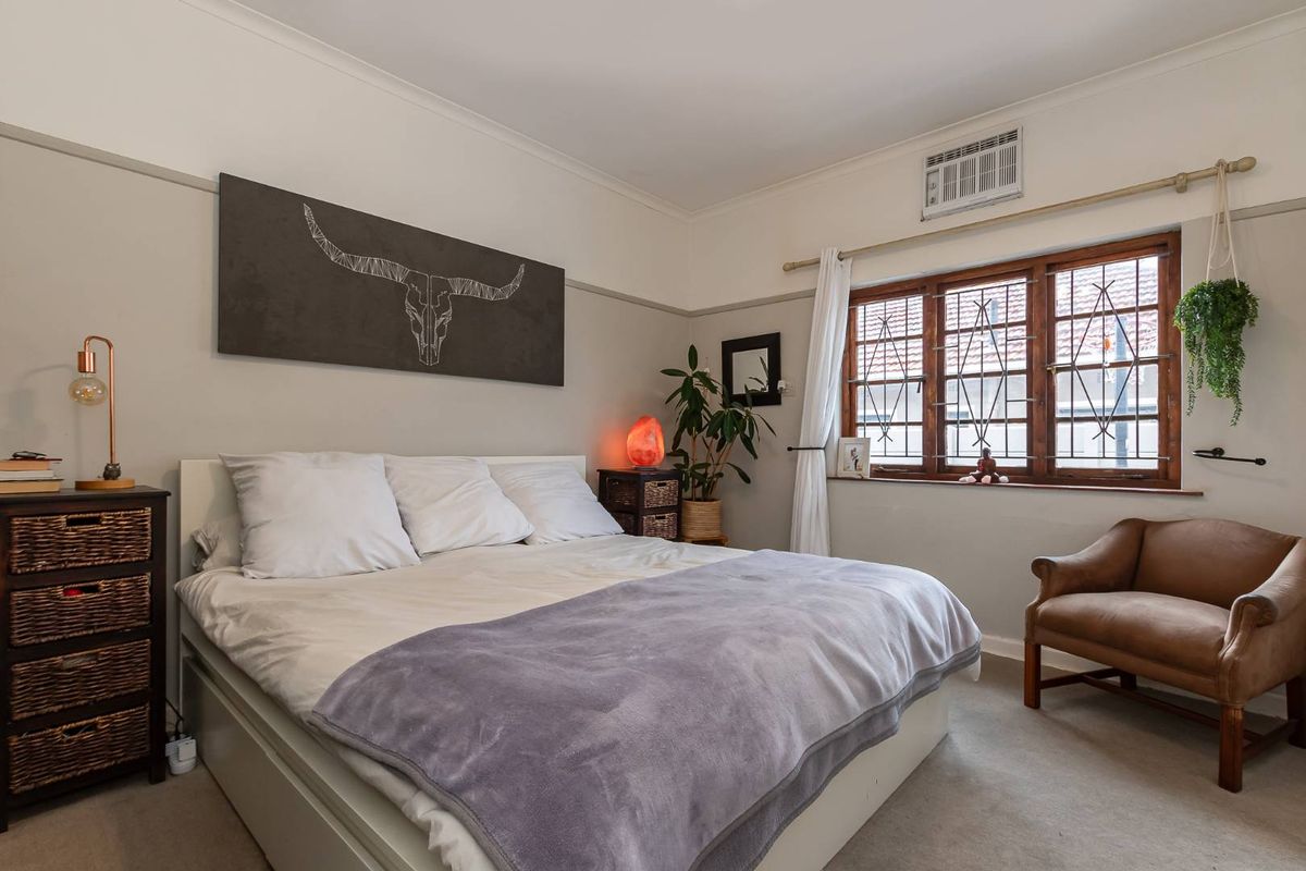 A well-lit bedroom featuring timber-framed windows with security bars, a wall-mounted air conditioning unit, and classic picture rail detailing.