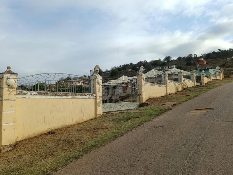 A street-level view of the property's perimeter wall, featuring decorative stone pillars and wrought iron fencing along the roadside.