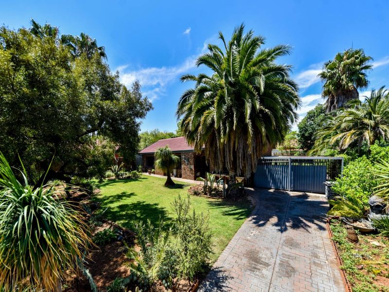 A well-maintained front exterior featuring a paved driveway, mature garden landscaping, and a brick facade with a tiled roof.