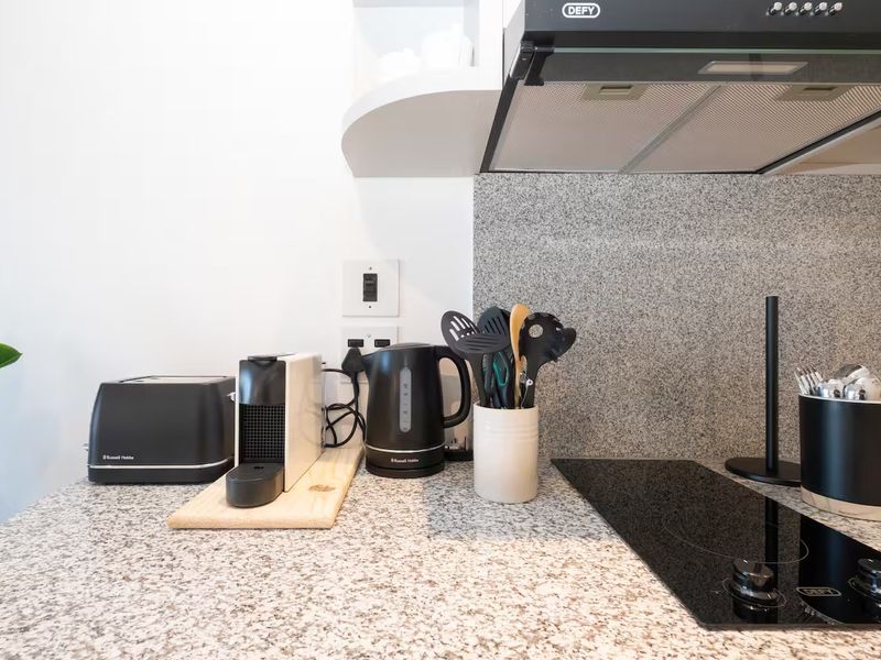 A clean, modern kitchen area featuring a granite countertop, matching backsplash, built-in electric hob, and an overhead extractor fan.