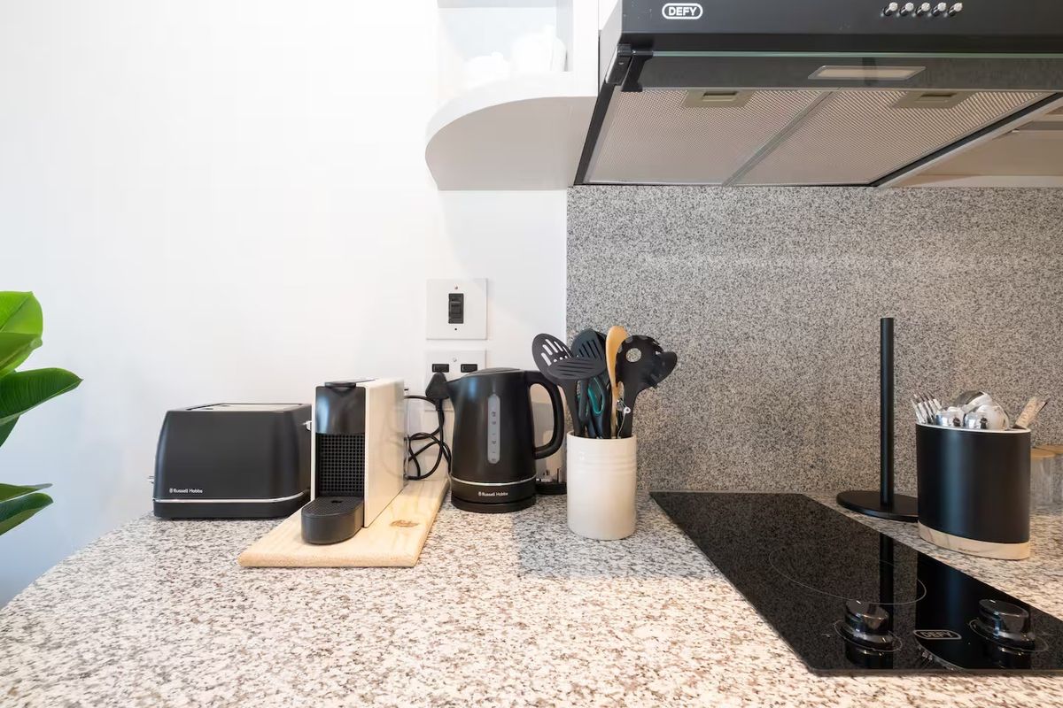 A clean, modern kitchen area featuring a granite countertop, matching backsplash, built-in electric hob, and an overhead extractor fan.