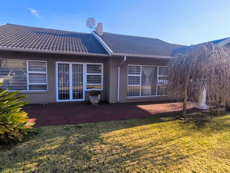Rear view of the house featuring a paved patio area, tiled roof, and secure aluminium window and door frames overlooking the garden.