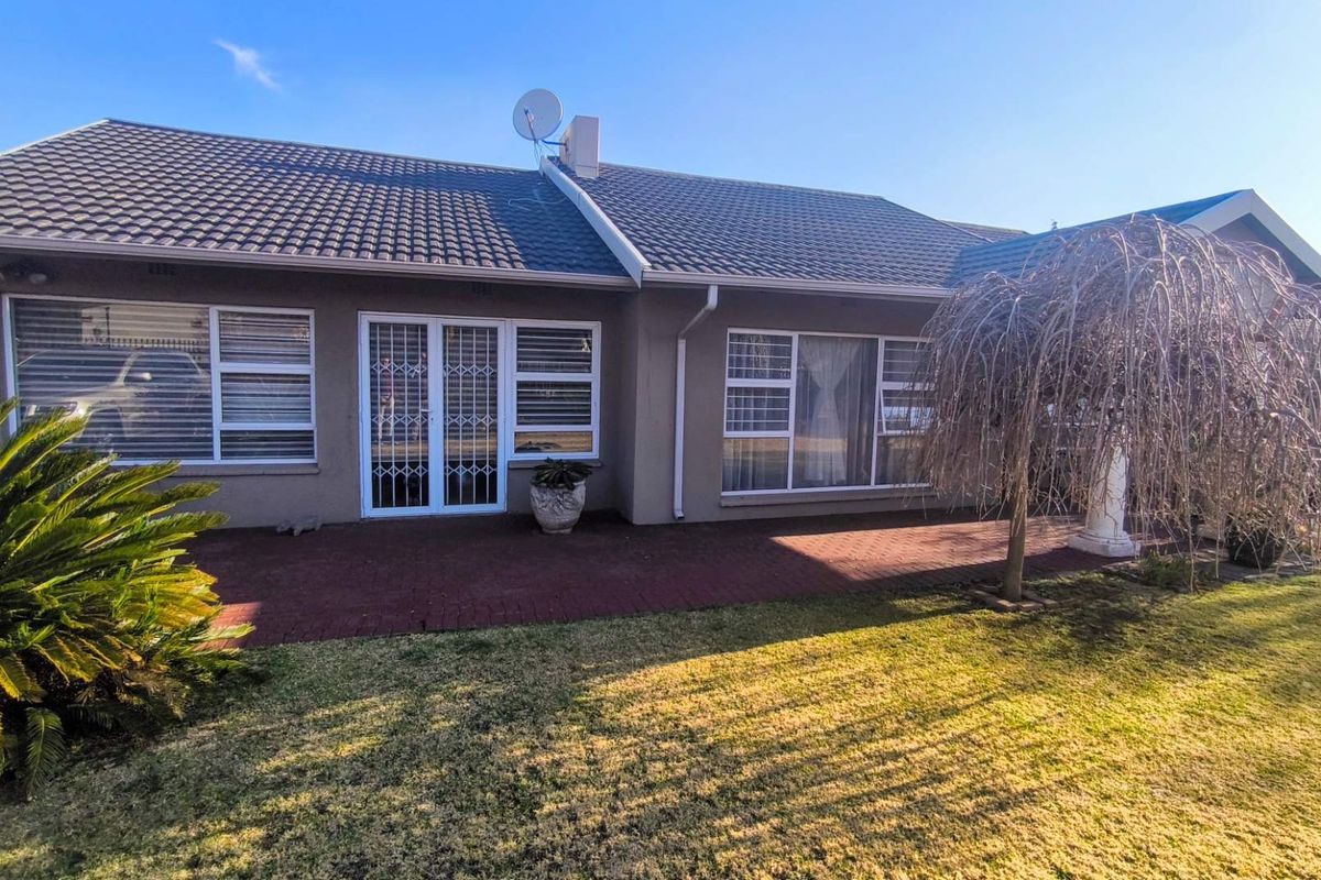 Rear view of the house featuring a paved patio area, tiled roof, and secure aluminium window and door frames overlooking the garden.