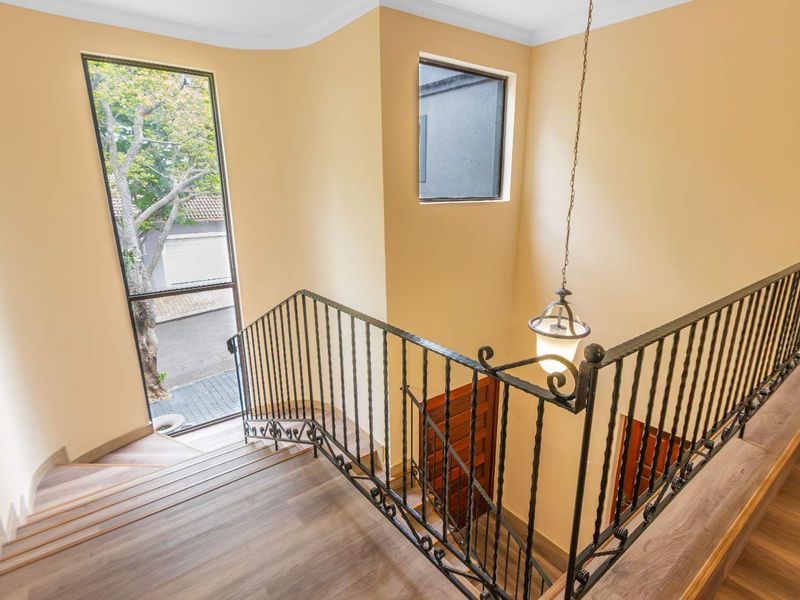 A bright hallway featuring a staircase with a decorative wrought iron balustrade, modern laminate flooring, and a tall window providing natural light.