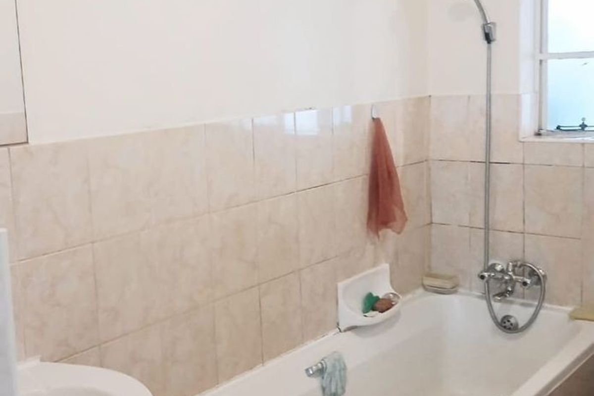 A functional bathroom featuring a standard bathtub with a wall-mounted shower head, a pedestal basin, and neutral wall tiling.