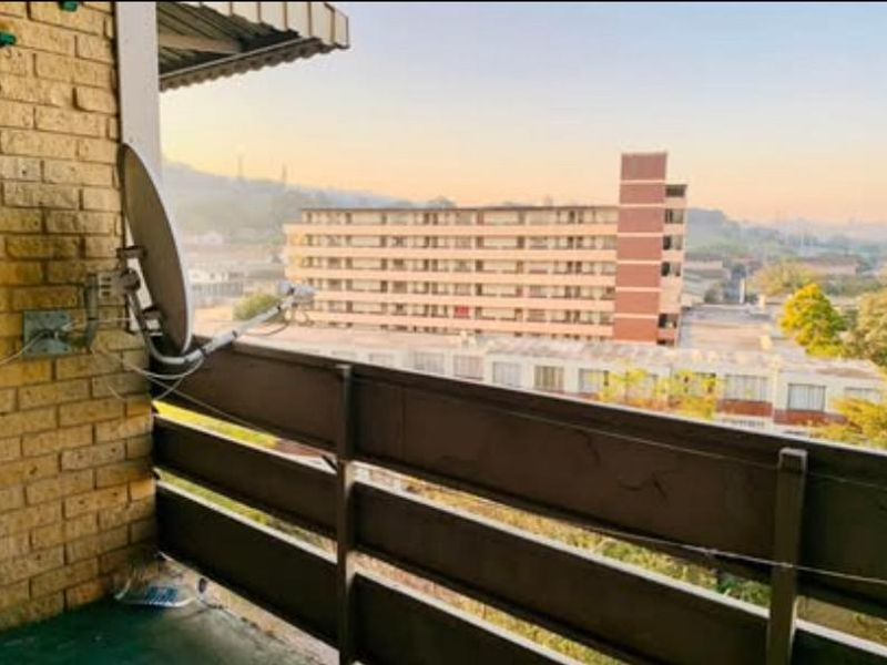 A balcony area featuring a brick wall, metal railing, and an installed satellite dish, offering an elevated view of the surrounding apartment complex.