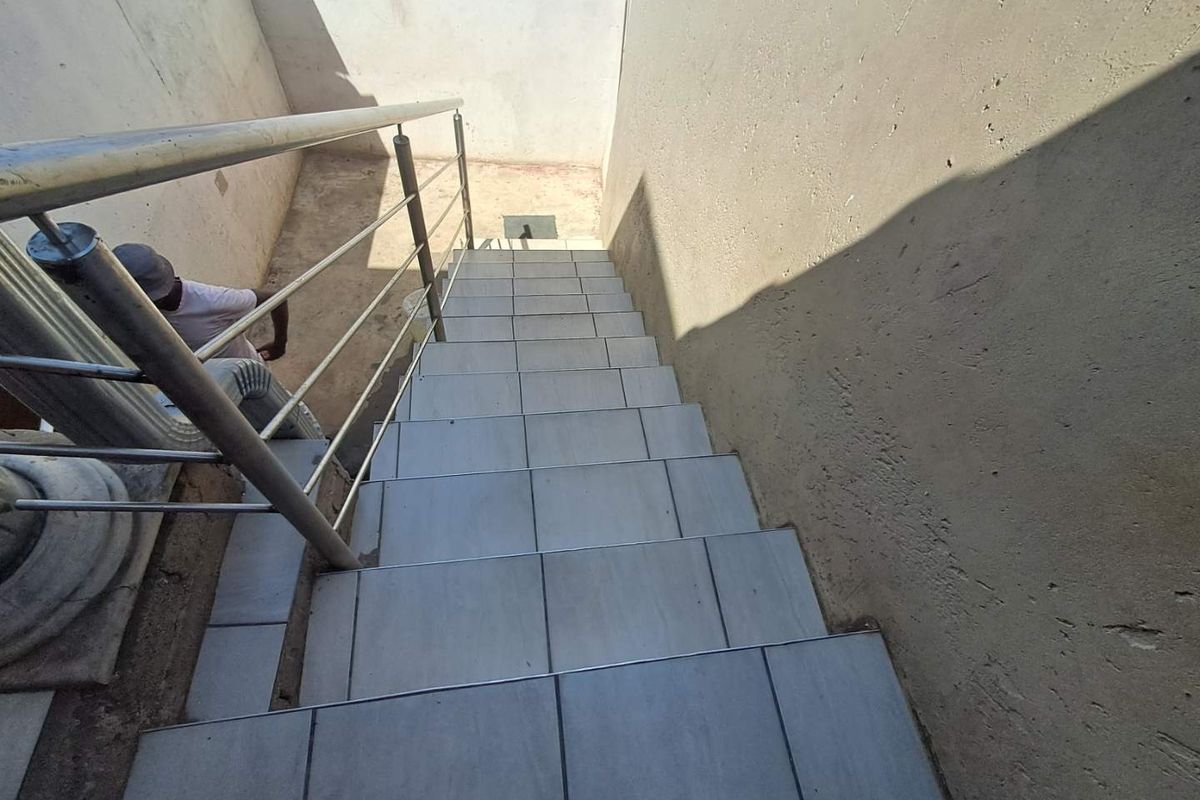 An outdoor staircase featuring tiled steps and a stainless steel handrail, leading down to a lower level area.