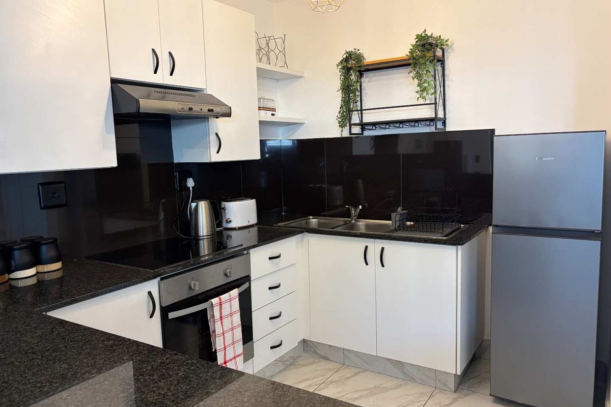 Modern kitchen featuring white cabinetry, black granite countertops, a glass splashback, built-in oven, electric hob, and tiled flooring.