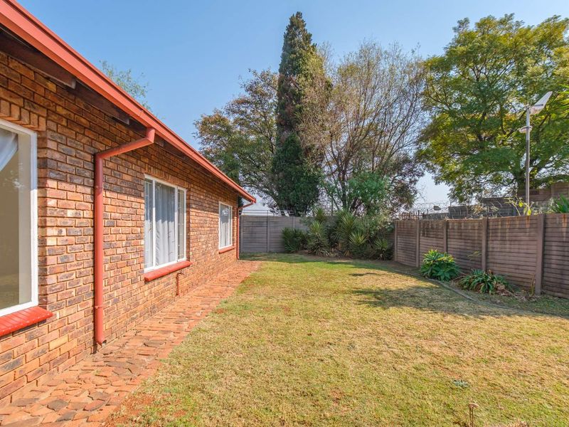 A private rear garden featuring a face brick townhouse exterior, a brick paved walkway, and a secure precast concrete boundary wall.