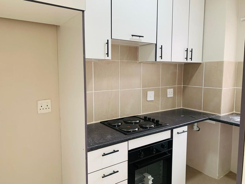 A compact kitchen featuring white cabinetry, dark laminate countertops, a built-in electric oven and hob, and neutral tiled backsplash.