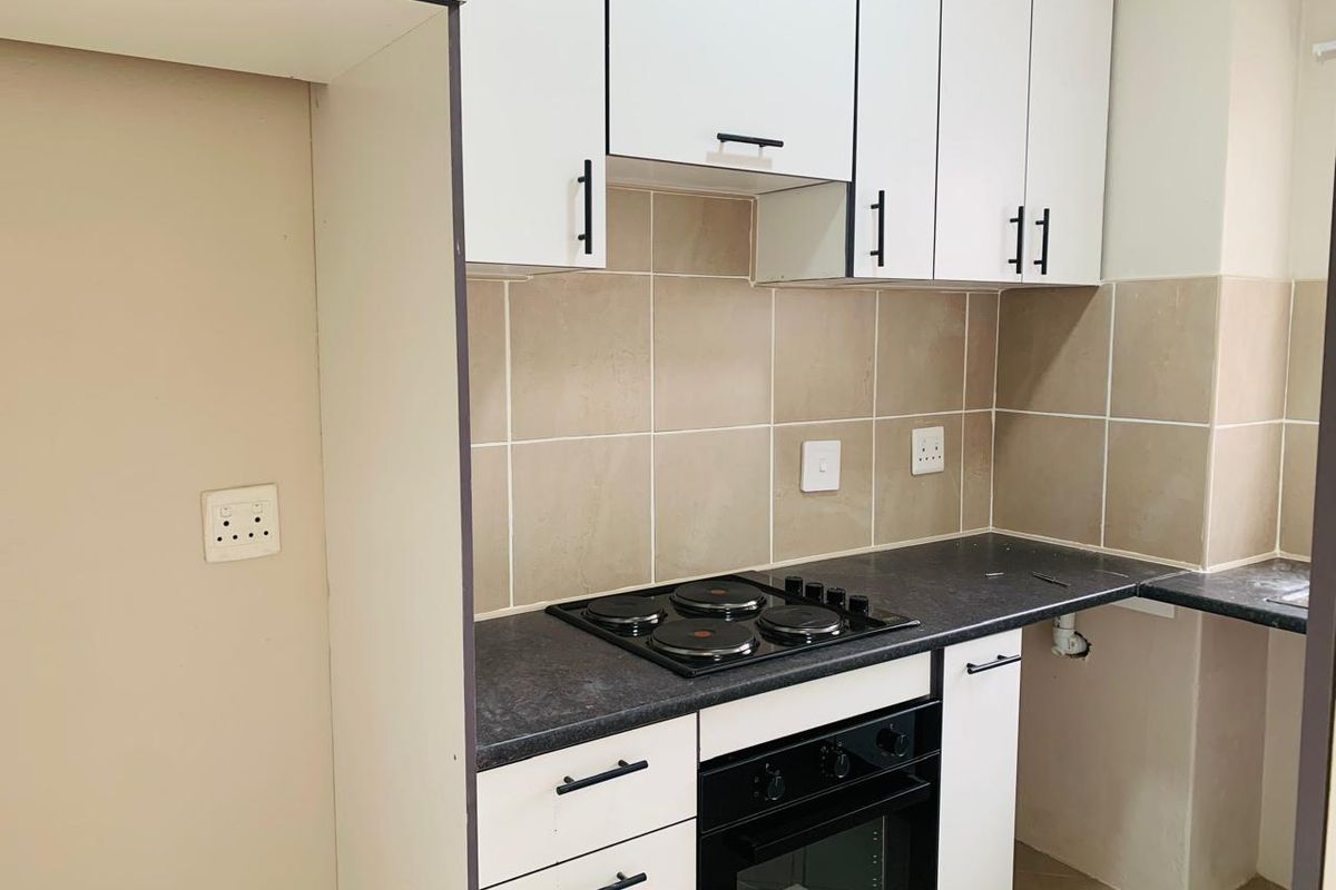 A compact kitchen featuring white cabinetry, dark laminate countertops, a built-in electric oven and hob, and neutral tiled backsplash.
