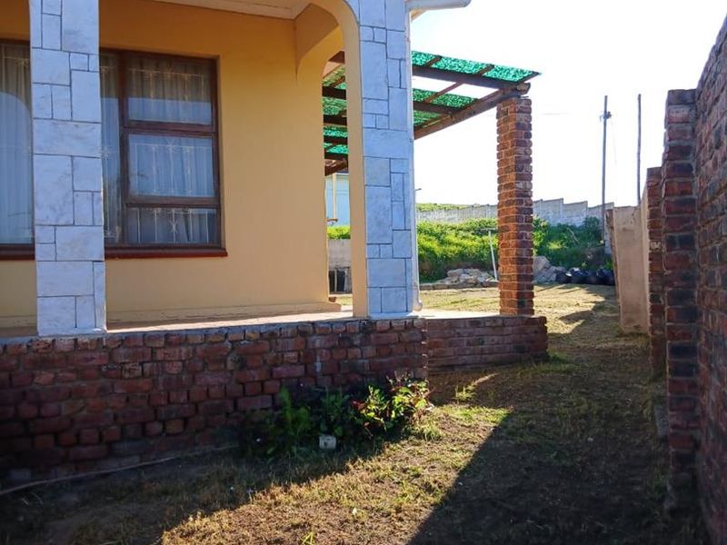 Rear view of the house featuring a covered patio area with brick pillars, stone cladding, and a surrounding brick boundary wall.