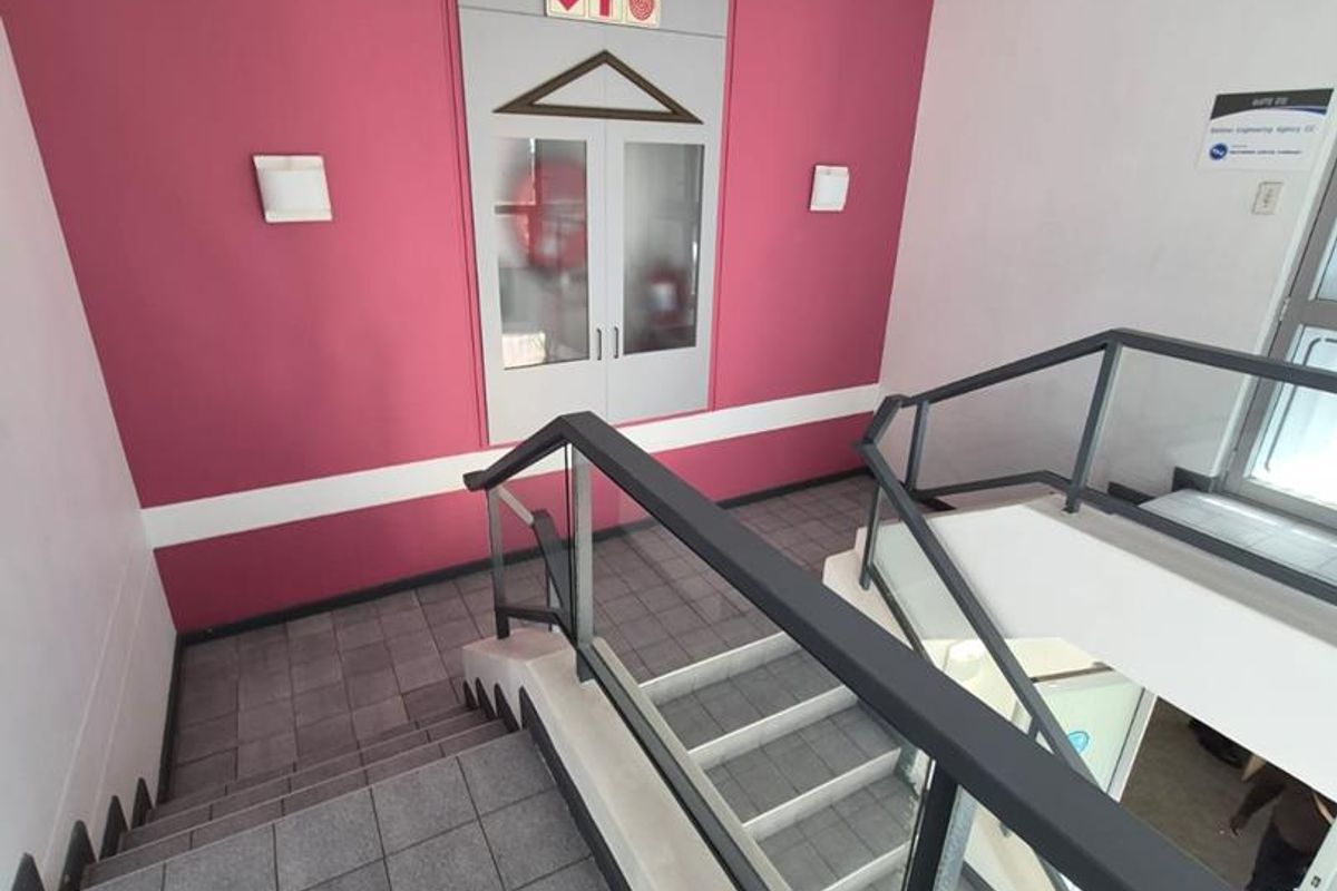 A clean, modern office stairwell featuring tiled flooring, a glass balustrade, and a recessed fire hose cabinet against a vibrant accent wall.