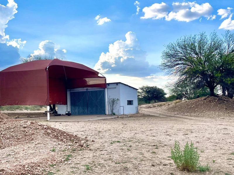 A commercial property featuring a metal shed structure with an attached shade cloth canopy, situated on a large, open, undeveloped land plot.
