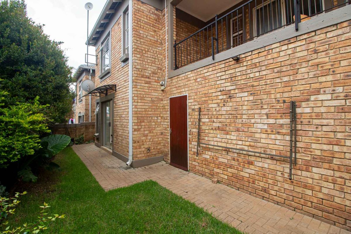 Rear exterior view of the townhouse featuring a paved patio area, brick facade, and a balcony with metal railings overlooking a small garden.