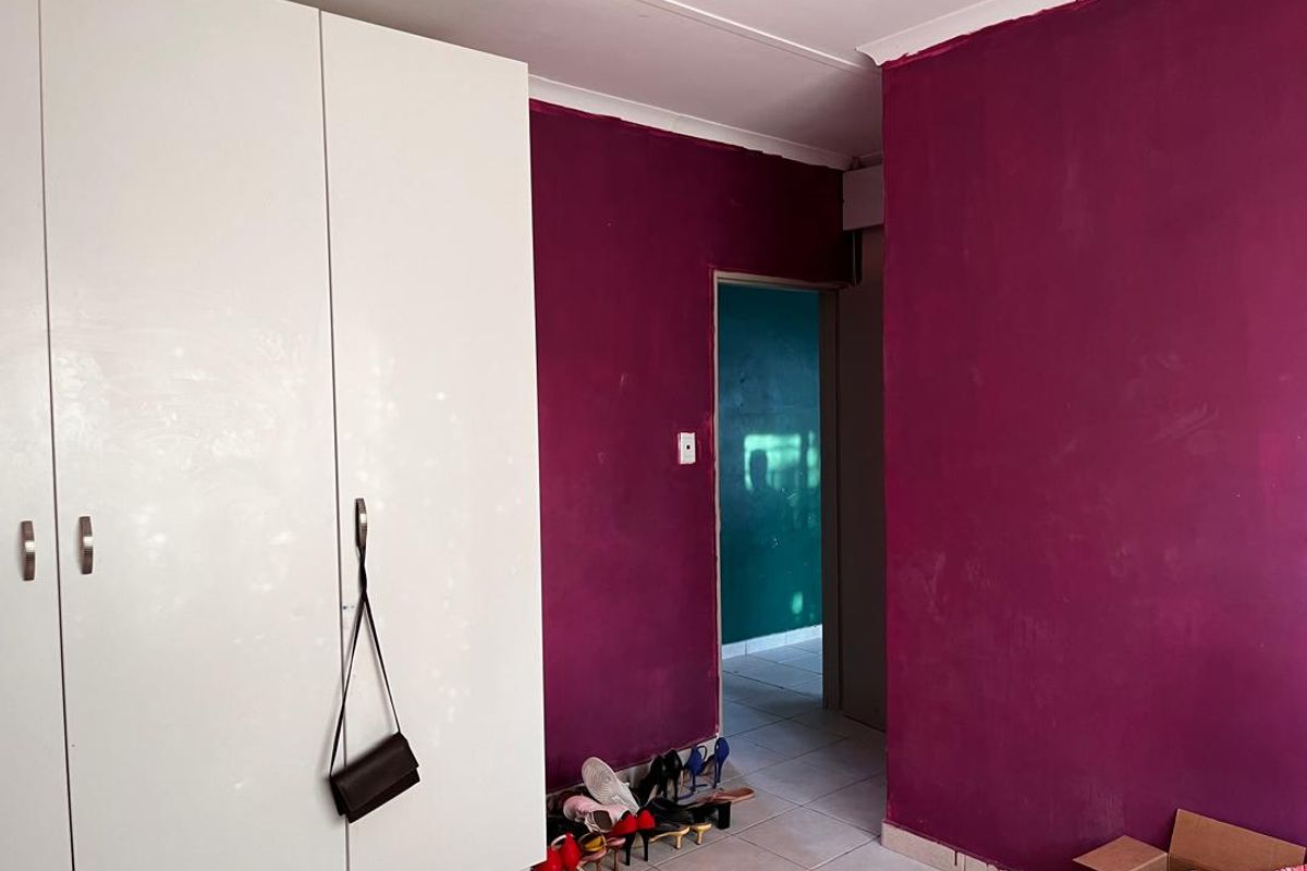 A bedroom interior featuring built-in white cabinetry and bold purple painted walls, with tiled flooring and access to an adjacent hallway.