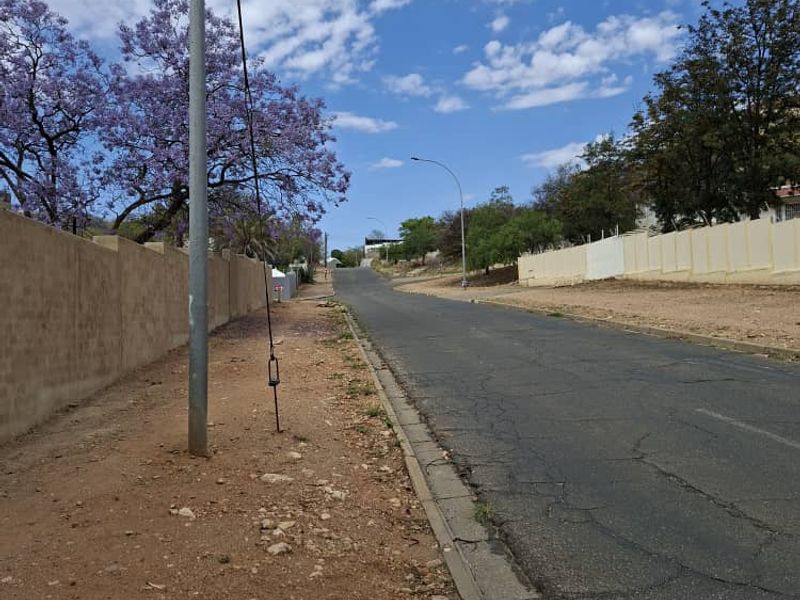 A view of the residential street showing the asphalt road, concrete curbing, and perimeter boundary walls along the property frontage.