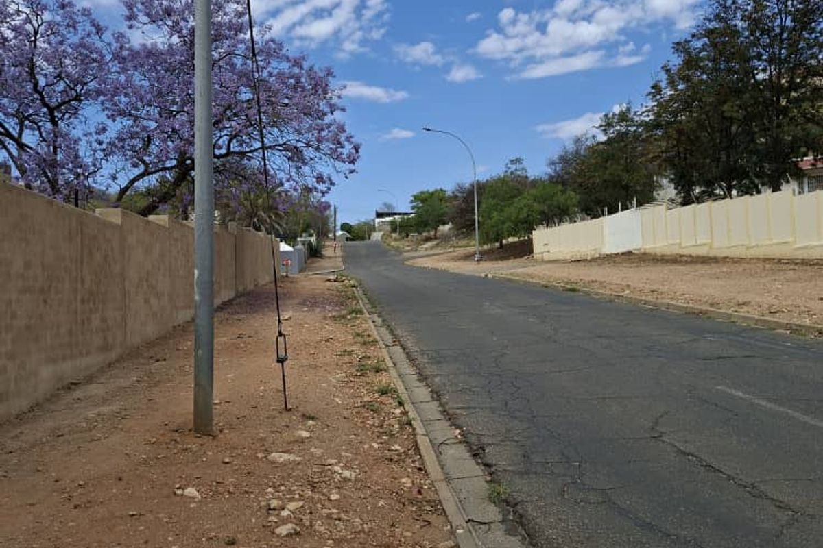 A view of the residential street showing the asphalt road, concrete curbing, and perimeter boundary walls along the property frontage.