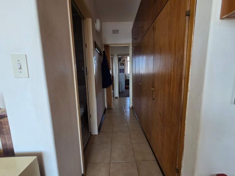 A functional hallway featuring tiled flooring and extensive built-in wooden cabinetry for storage, providing access to adjacent rooms.