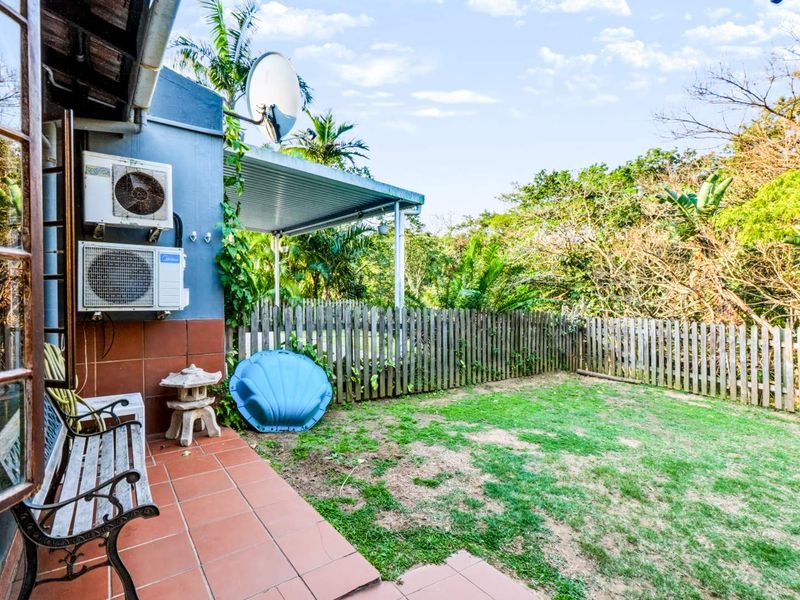 Rear exterior view of the townhouse featuring a tiled patio area, air conditioning units, and a private garden enclosed by a wooden picket fence.