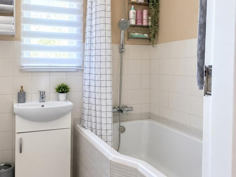 A clean and functional bathroom featuring a vanity basin, a bathtub with a shower mixer, and tiled wall finishes.