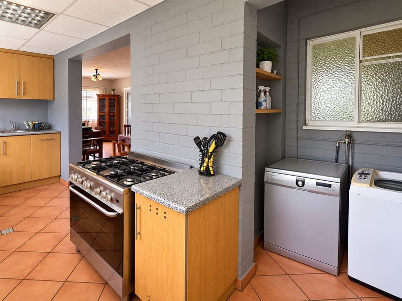 A functional kitchen featuring a gas stove, tiled flooring, and built-in cabinetry, with an adjacent laundry area and views into the dining room.