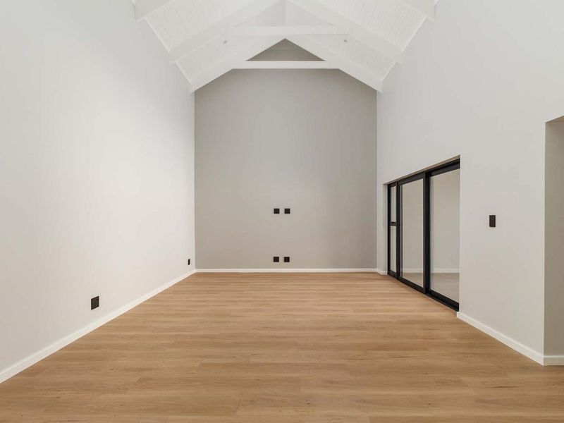Spacious living area featuring a high vaulted ceiling with exposed trusses, modern laminate flooring, and large sliding glass doors providing natural light.