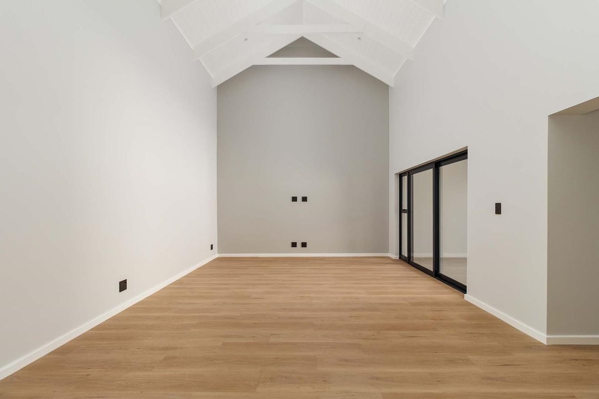 Spacious living area featuring a high vaulted ceiling with exposed trusses, modern laminate flooring, and large sliding glass doors providing natural light.