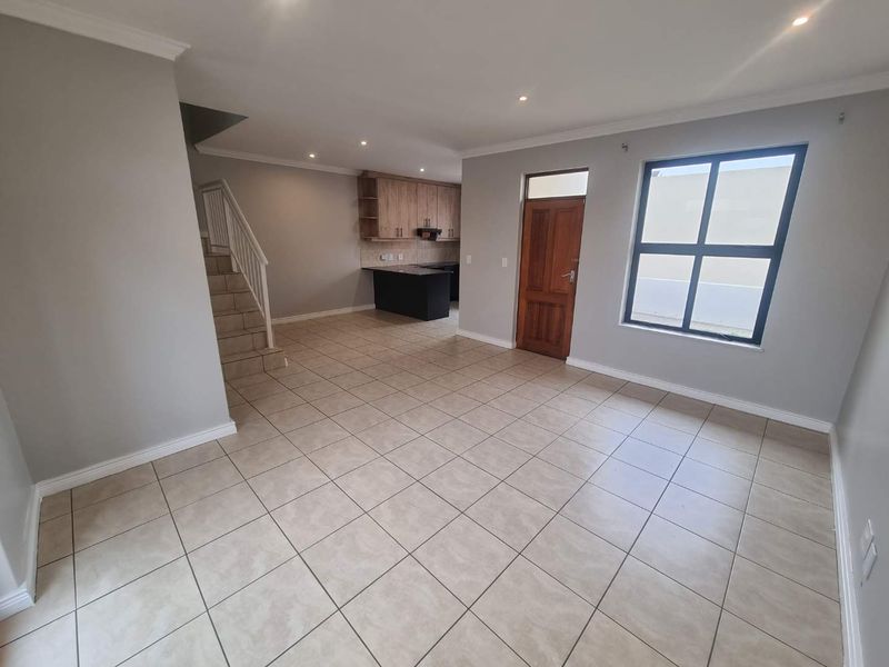 Spacious open-plan living area featuring tiled floors, a staircase, and an integrated kitchen with modern cabinetry and recessed lighting.