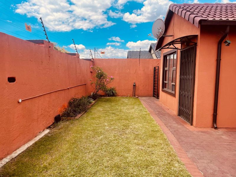 A private rear garden featuring a paved walkway, lawn area, and perimeter wall with electric fencing.