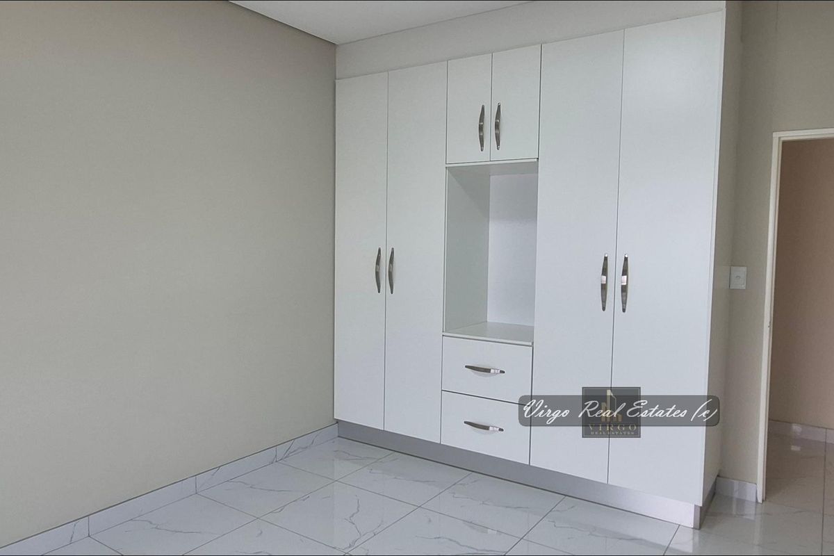 A clean, modern bedroom featuring white built-in cupboards with integrated shelving and drawers, complemented by light-colored tiled flooring.