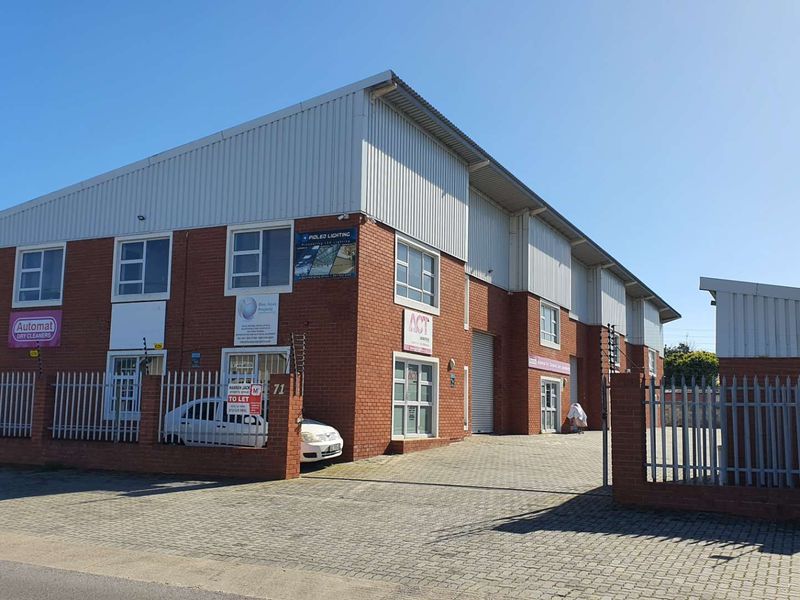 A commercial industrial property featuring a brick facade, metal roofing, paved driveway, and secure perimeter fencing with electric security measures.