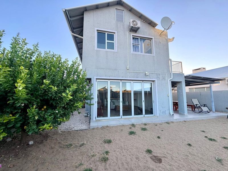 Rear view of a two-story house featuring large aluminium stacker doors leading to a tiled patio area and an installed air conditioning unit.