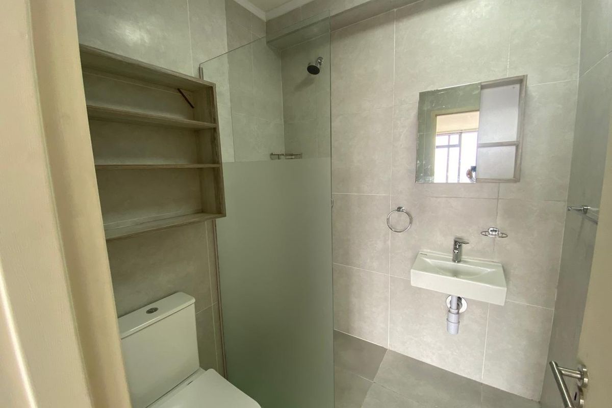 Modern bathroom featuring a wall-mounted basin, glass shower screen, toilet, and built-in shelving with neutral floor-to-ceiling tiling.