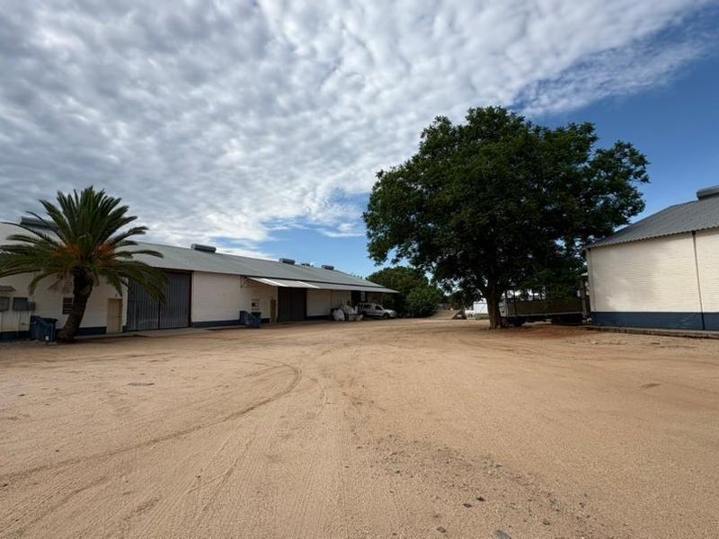 A wide view of a commercial property yard featuring large warehouse buildings with corrugated roofing and painted brick exteriors.