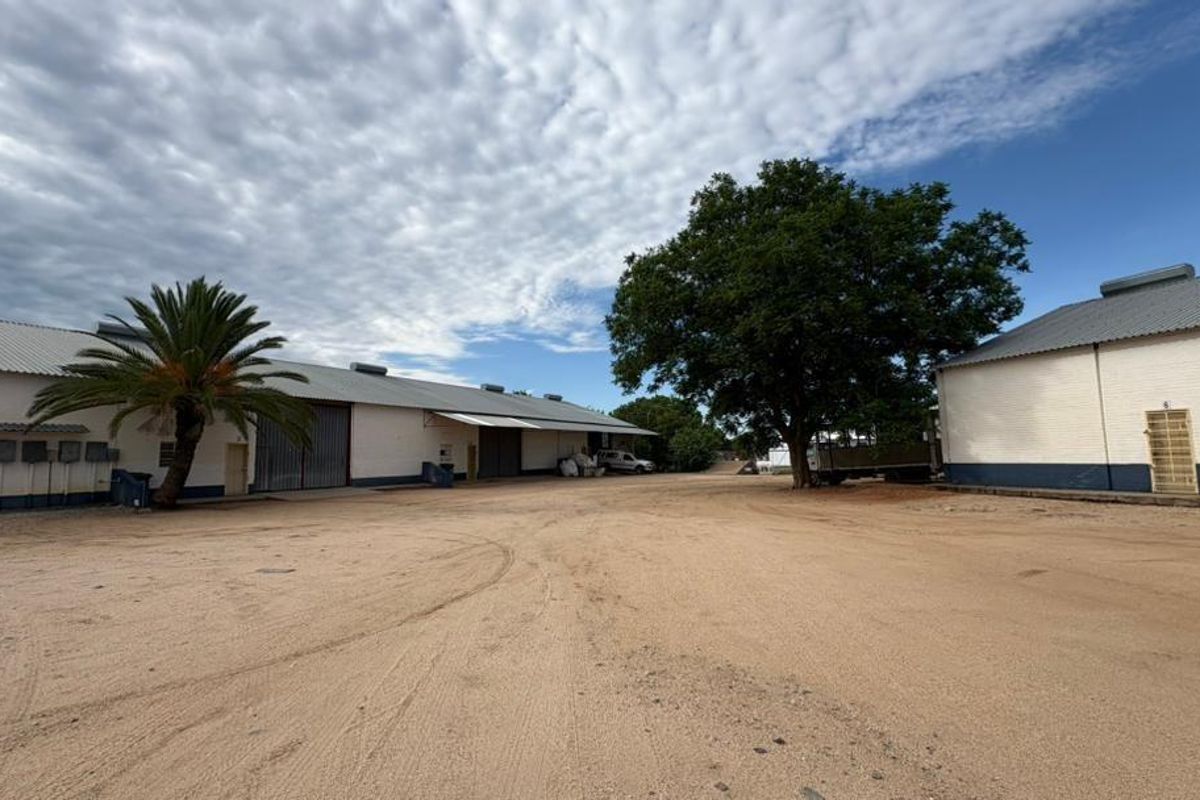 A wide view of a commercial property yard featuring large warehouse buildings with corrugated roofing and painted brick exteriors.